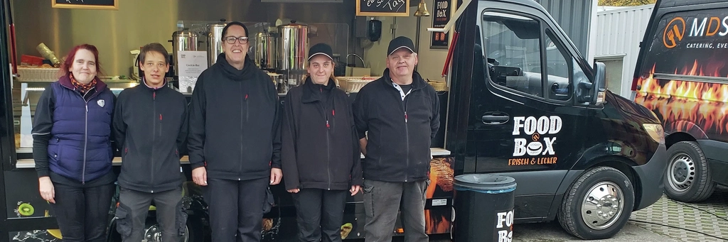 Fünf Personen stehen vor der Food Box, ein umgebauter schwarzer Sprinter mit Essensausgabe