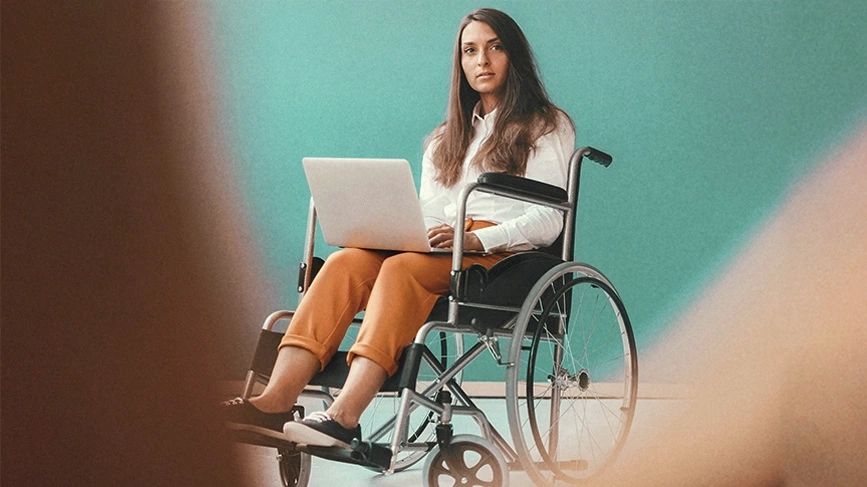 Eine Frau sitzt in einem Leichtgewichtrollstuhl. Sie hat einen Laptop auf dem Schoß.