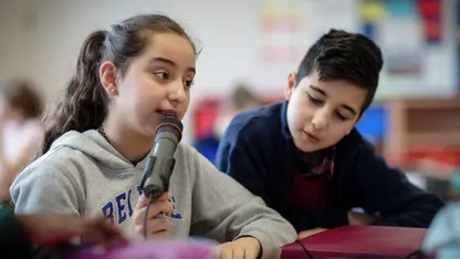 Ein Mädchen in einer Schulklasse spricht ins Mikrofon.
