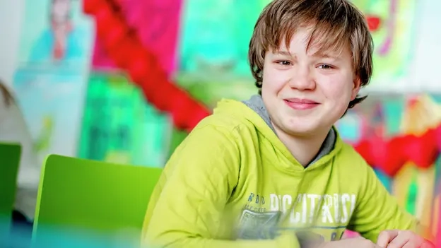 Ein Schüler sitzt fröhlich an einem Tisch.