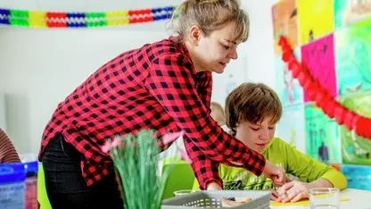 Eine Betreuerin zeigt einem Schüler etwas. Beide lächeln.