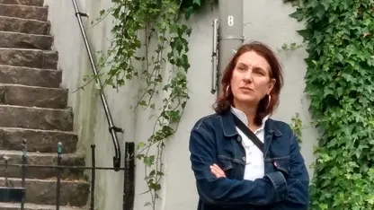 Frau lehnt lässig an einem Laternenpfahl und hat die Arme vor der Brust verschränkt