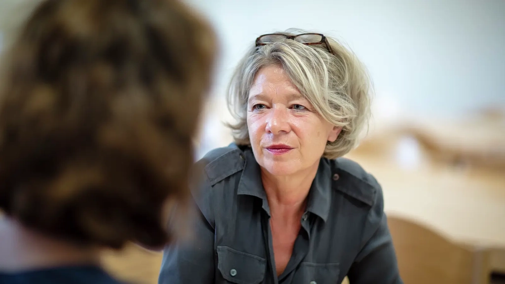 Zwei Frauen sitzen sich in einem Klassenzimmer gegenüber und scheinen sich zu unterhalten. 