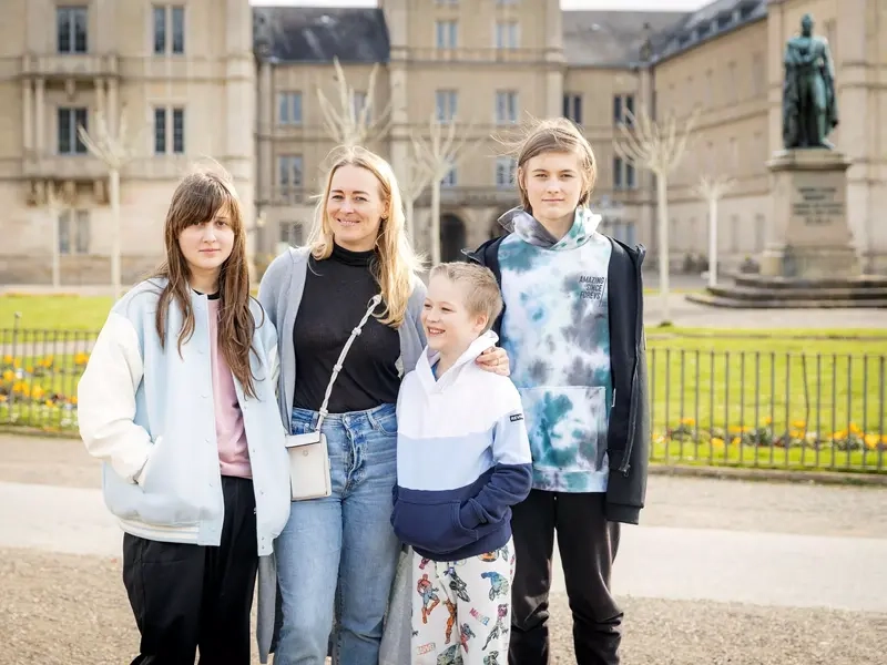 Familienbild einer Mutter mit ihren drei Kindern vor einer Schlossanlage.
