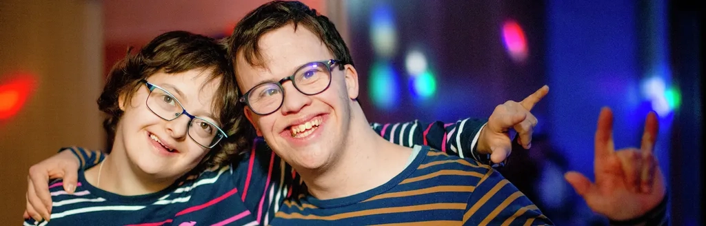 Zwei junge Menschen liegen sich in den Armen und machen mit ihrer linken Hand die Geste für "i love you".