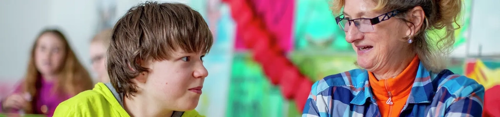 Ein Schüler und eine Lehrerin schauen sich freundlich an.