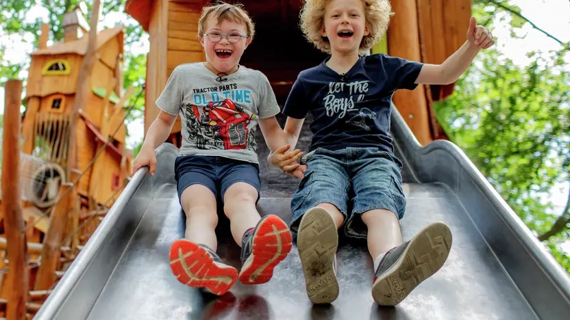 Zwei Jungs, einer davon mit Downsyndrom, auf einer Rutsche