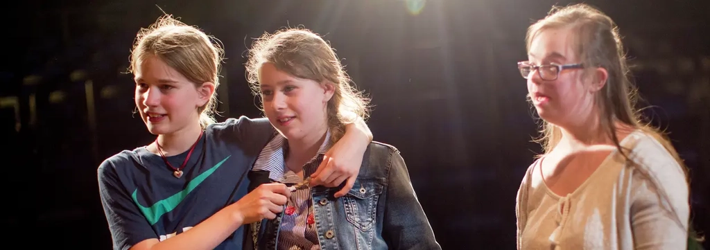 Drei Mädchen stehen nebeneinander. Zwei umarmen sich. Das dritte Mädchen steht etwas abseits.