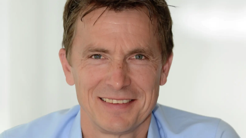 Porträt von Volker Anneken, ein Mann im mittleren Alter mit blauem Hemd und blonden Haaren