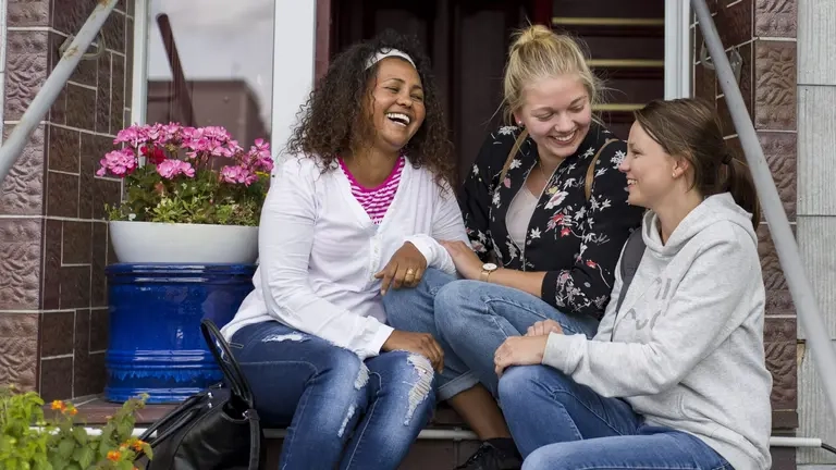 Drei junge Frauen sitzen auf einer Eingangstreppe und lachen.