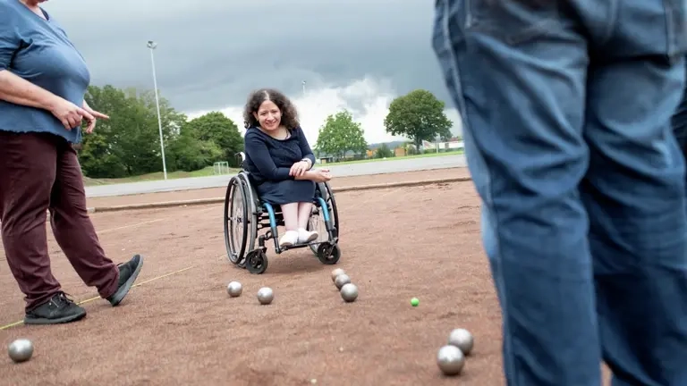 Zwei Frauen spielen Boule, eine sitzt in einem Rollstuhl