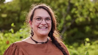 Dr. Lea Schulz. Eine Frau mit langen dunklen geflochtenen Haaren und großen Ohrringen.