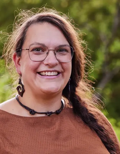 Dr. Lea Schulz. Eine Frau mit langen dunklen geflochtenen Haaren und großen Ohrringen.