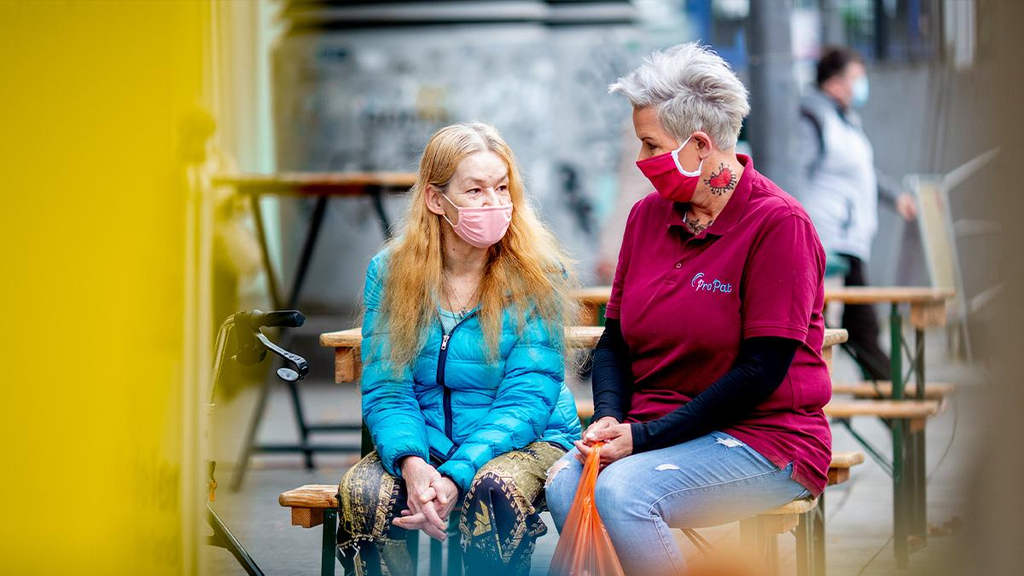 Zwei Frauen sitzen auf einer Bank und unterhalten sich.