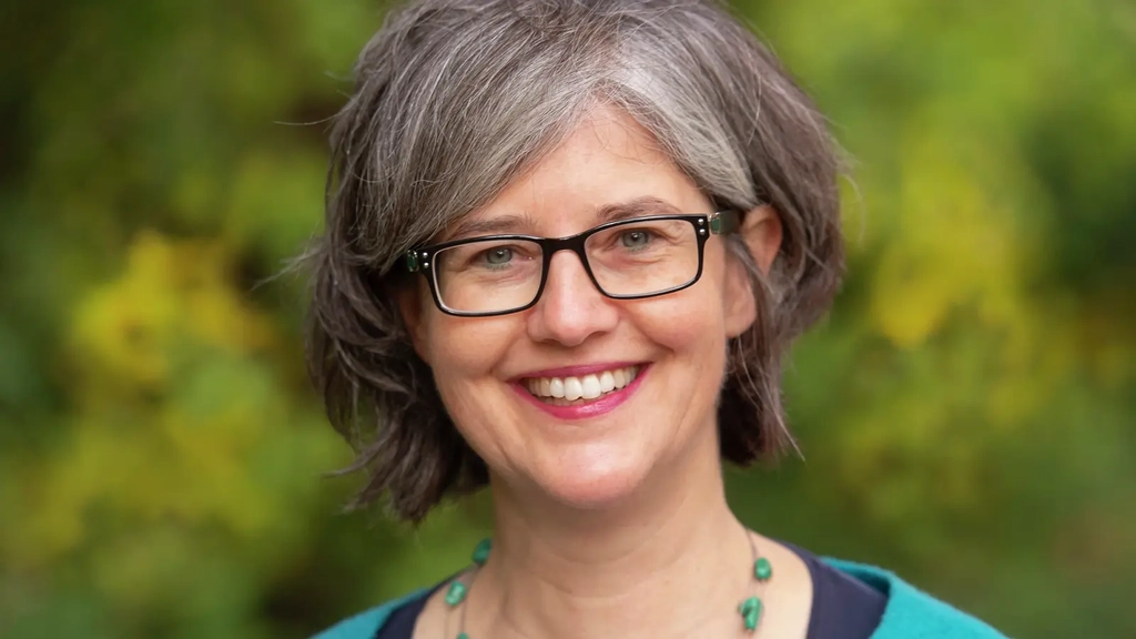 Birgit Mock, eine Frau mit schwarz-grauen Haaren und Brille, trägt einen blauen Blazer und lächelt in die Kamera.