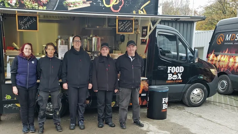 Fünf Personen stehen vor der Food Box, ein umgebauter schwarzer Sprinter mit Essensausgabe