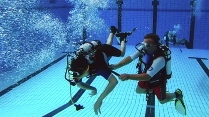 Zwei Taucher unter Wasser. Einer von ihnen hat eine Behinderung und wird vom anderen unterstützt.