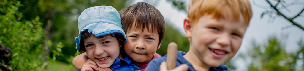 Drei Kinder in der Natur lachen in die Kamera.