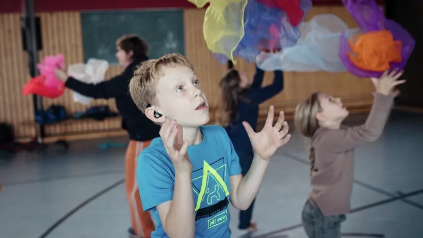 Ein Junge mit Hörgerät jongliert mit bunten Tüchern 