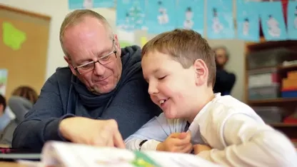 Mann unterstützt ein Kind beim Lesen