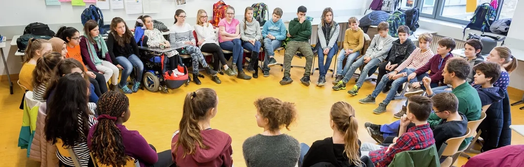 Etwa 30 Jugendliche sitzen im Stuhlkreis mit einem Erwachsenen zusammen.