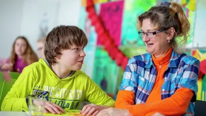 Ein Schüler und eine Lehrerin schauen sich freundlich an.