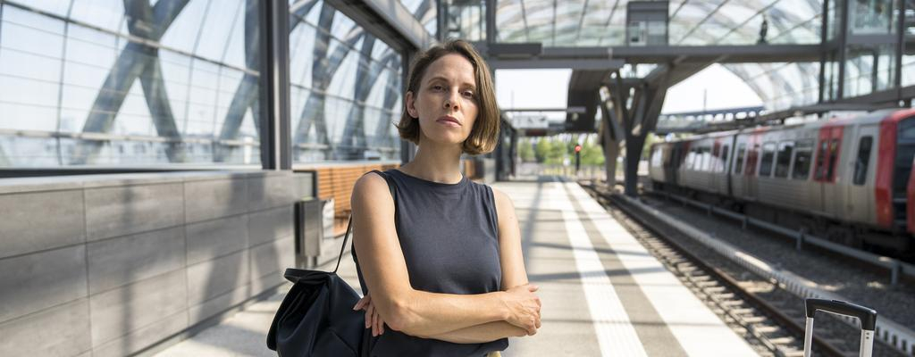 Ein Potraitbild von Kassandra Wedel. Sie steht an einem Bahnsteig und hält die Arme verschränkt vor dem Körper.