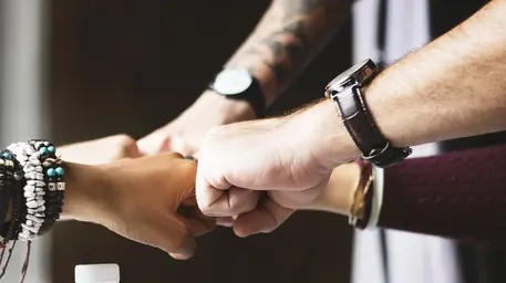 Eine Gruppe von Menschen ballt über einem Tisch die Hände zusammen.