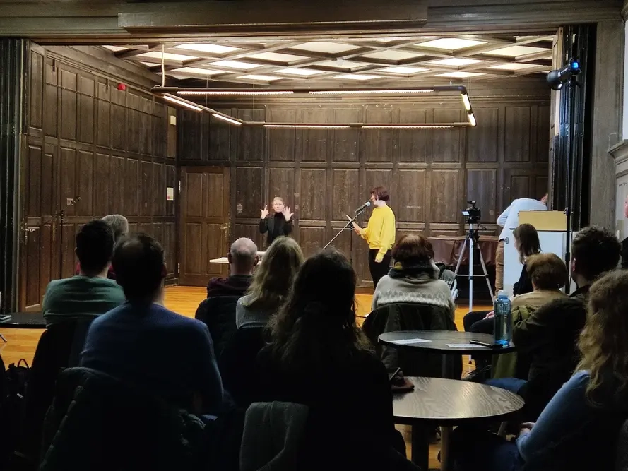 Zuhörer hören einer Frau beim Poetry Slam zu. Eine Frau gebärdet den Text.
