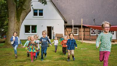 Mehrere Kinder laufen aus einem alten Bauernhaus auf eine Wiese