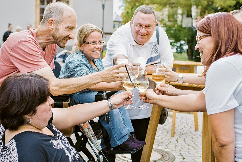 Mehrere Menschen mit und ohne Behinderung stoßen im Freien an 