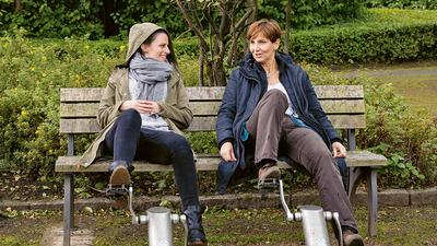 Zwei Frauen sitzen im Grünen auf der Bank und treten dort installierte Fitnessgeräte