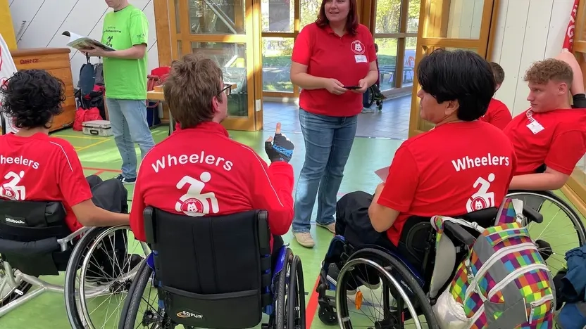 Eine Gruppe von Rollstuhlfahrern in roten Trikots sprechen miteinander