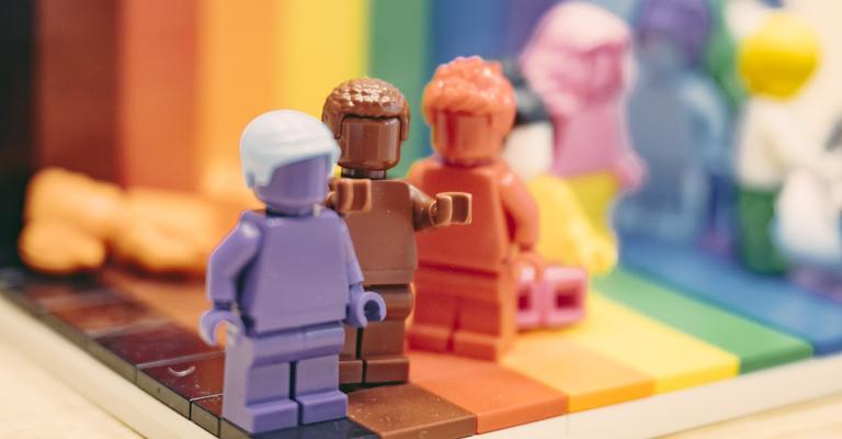Mehrere bunte Legofiguren vor einem regenbogenfarbenen Hintergrund