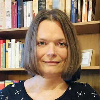 Eine junge Frau mit Pagenkopf-Haarschnitt steht vor einem Bücherregal