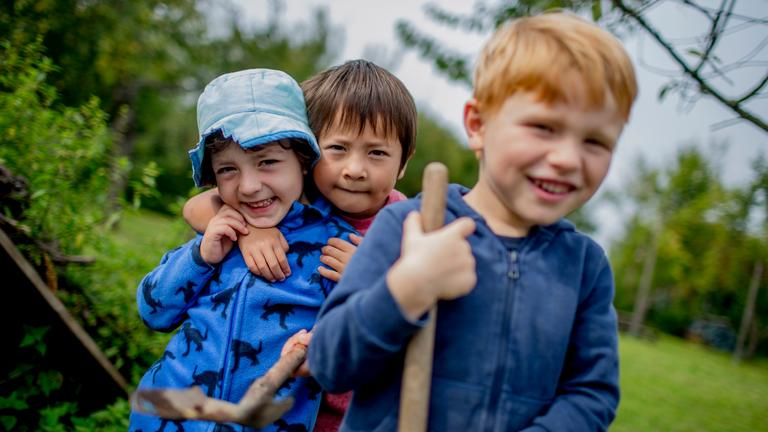 Drei Kinder in der Natur lachen in die Kamera.