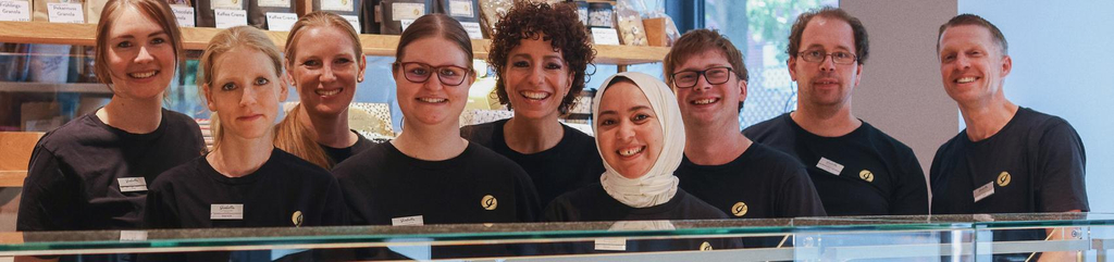 Gruppenbild der Mitarbeiter*innen der Patisserie. Im Vordergrund ist die Glastheke mit der Kuchenauswahl zu sehen. 