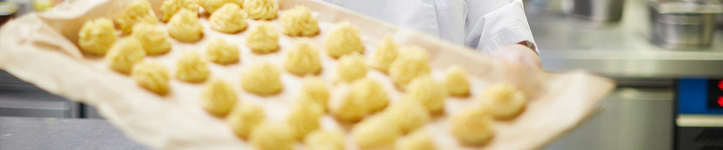 Eine Mitarbeiterin hält ein Backblech mit kleinen Kuchen in der Hand.