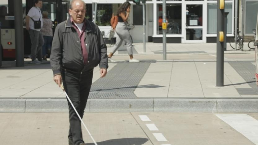 Ein Mann mit Blindenstock überquert eine Straße vor einem Bus.