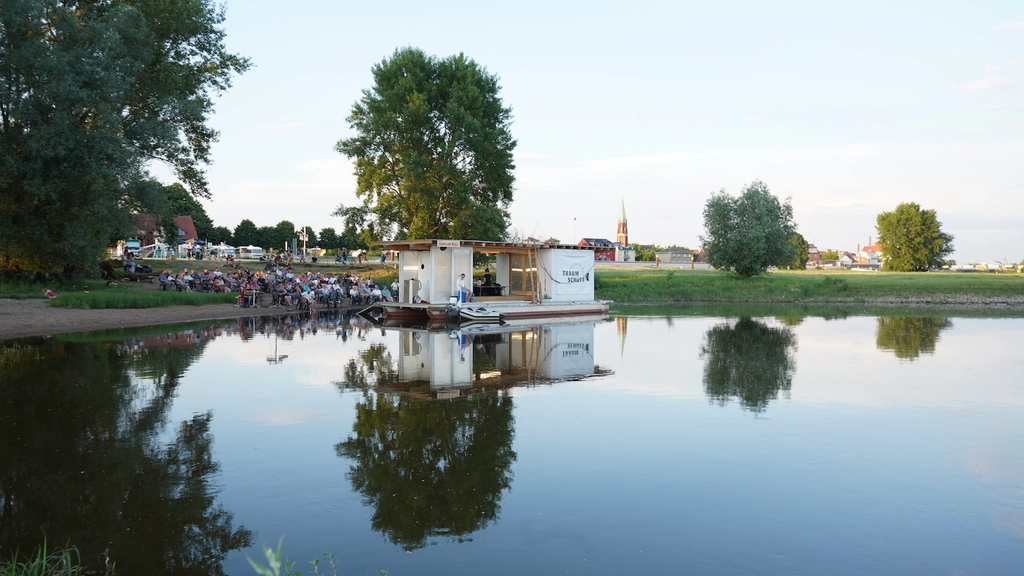 Das Traumschüff liegt in Dömitz vor Anker. Das Publikum sitzt am Ufer und verfolgt die Vorstellung.