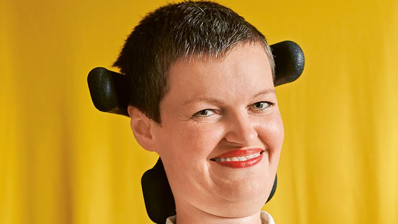 Eine Frau mit kurzen Haaren im Rollstuhl lächelt